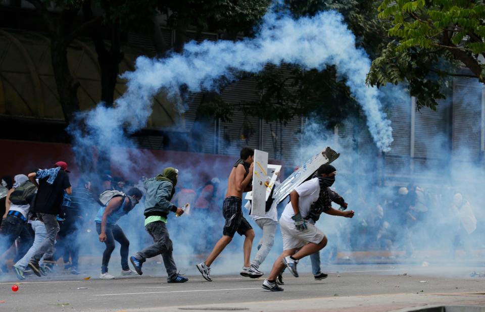 Demonstrators run from the teargas fired by Bolivarian National Guards officers during an anti-government protest in Caracas, Venezuela, Sunday, March 2, 2014. Since mid-February, anti-government activists have been protesting high inflation, shortages of food stuffs and medicine, and violent crime in a nation with the world's largest proven oil reserves. (AP Photo/Fernando Llano)