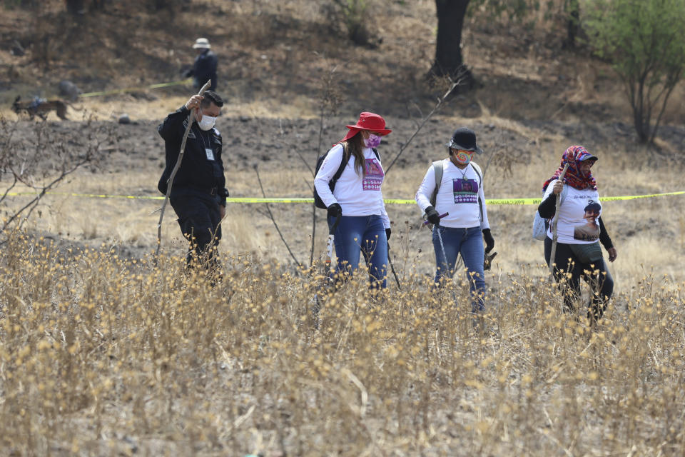 A police officer escorts women carrying digging tools at the site where a clandestine crematorium was found in Tlahuac, on the edge of Mexico City, Wednesday, May 1, 2024. Third from right is Jacqueline Palmeros who has been searching for her disappeared daughter since 2020 in Mexico City, and second from right is María de Jesús Soria whose daughter disappeared in Veracruz in 2016, and whose remains were turned over to her in 2022. (AP Photo/Ginnette Riquelme)