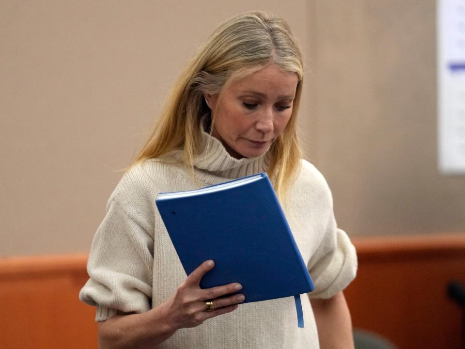 Gwyneth Paltrow walks in a courtroom carrying a blue notebook