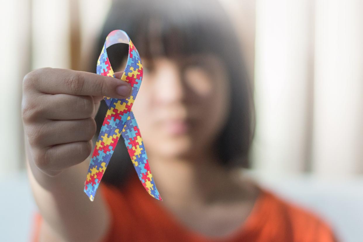 A young girl with Autism holds a ribbon symbol of colorful pieces of jigsaw together to raise awareness about people with Autism Spectrum Disorder throughout the world.