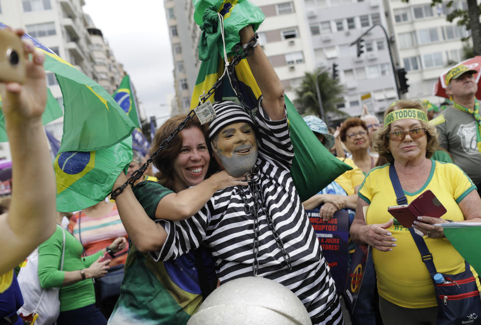 A man wearing a prison costume and mask of Brazil's former President Luiz Inacio Lula da Silva poses for photos with anther person grasping his neck, during a rally in support of the government's "Car Wash" investigation into corruption on Copacabana beach, Rio de Janeiro, Brazil, Sunday, Aug. 25, 2019. Da Silvia is currently serving a prison sentence for corruption. (AP Photo/Silvia Izquierdo)