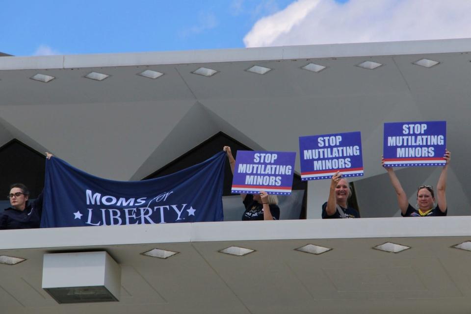 Demonstrators from Moms for Liberty hold protest signs on the roof of the North Carolina Legislative Building, Wednesday, Aug. 16, 2023, in Raleigh, N.C. The state legislature's Republican supermajority will attempt later Wednesday to override the Democratic governor's veto of a gender-affirming care ban for minors.