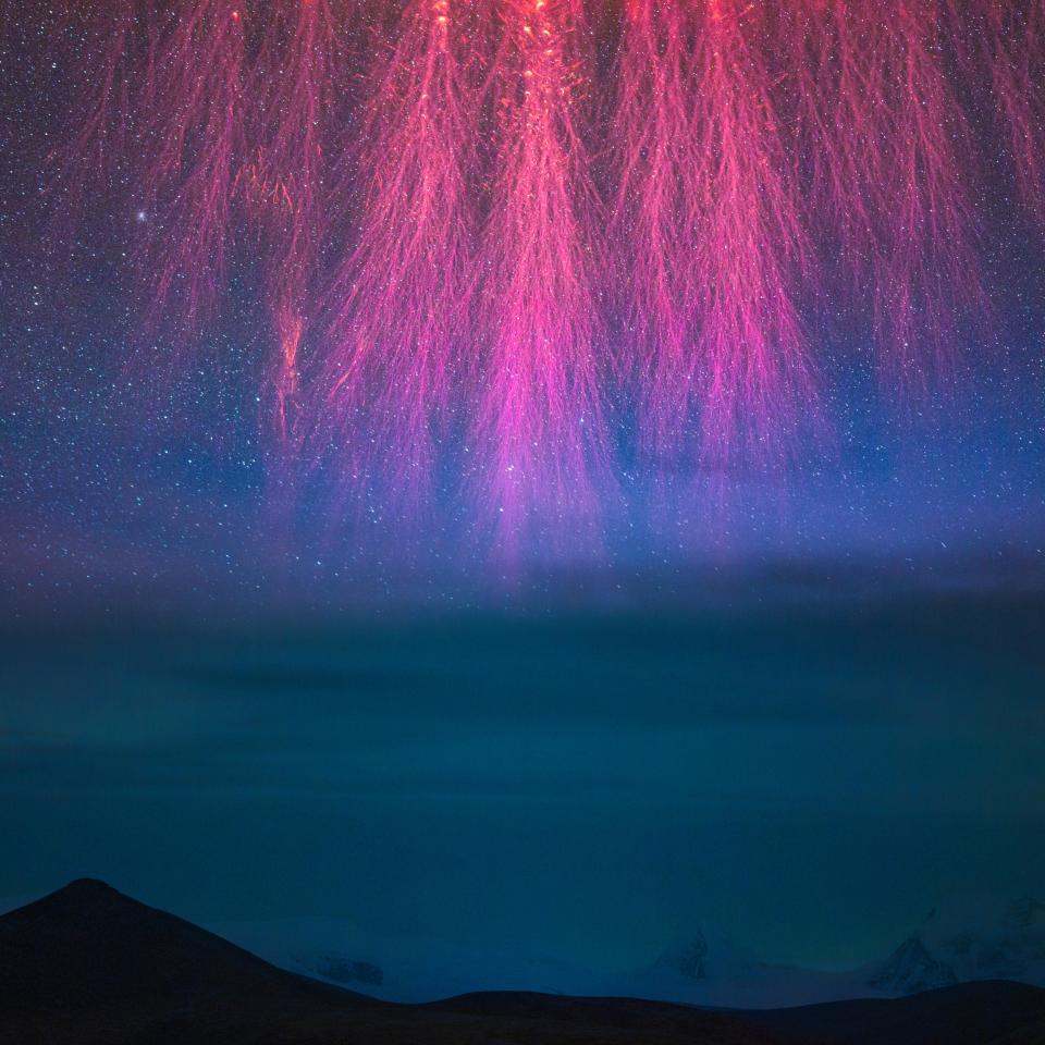 red/pink bolts with many branches reach down from the image top like lightning strikes above dark mountains