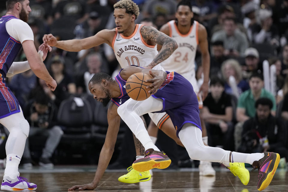 Phoenix Suns forward Kevin Durant, front, is tripped up as he drives around San Antonio Spurs forward Jeremy Sochan (10) during the second half of an NBA basketball game in San Antonio, Monday, March 25, 2024. (AP Photo/Eric Gay)