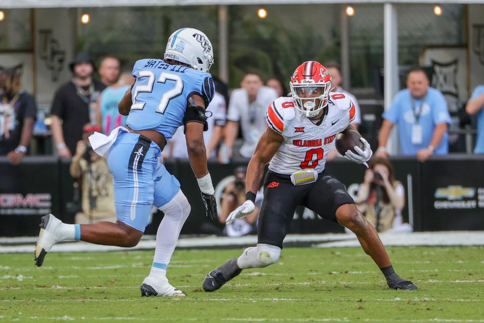 Nov 11, 2023; Orlando, Florida, USA; Oklahoma State Cowboys running back Ollie Gordon II (0) runs the ball in front of UCF Knights linebacker Walter Yates III (27) during the first quarter at FBC Mortgage Stadium. Mandatory Credit: Mike Watters-USA TODAY Sports