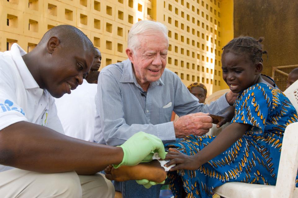 Former President Jimmy Carter consoles a young patient having a worm removed from her body in Savelugu, Ghana, in 2007. Since 1986, efforts by the Carter Center against Guinea worm disease has led to near eradication.
