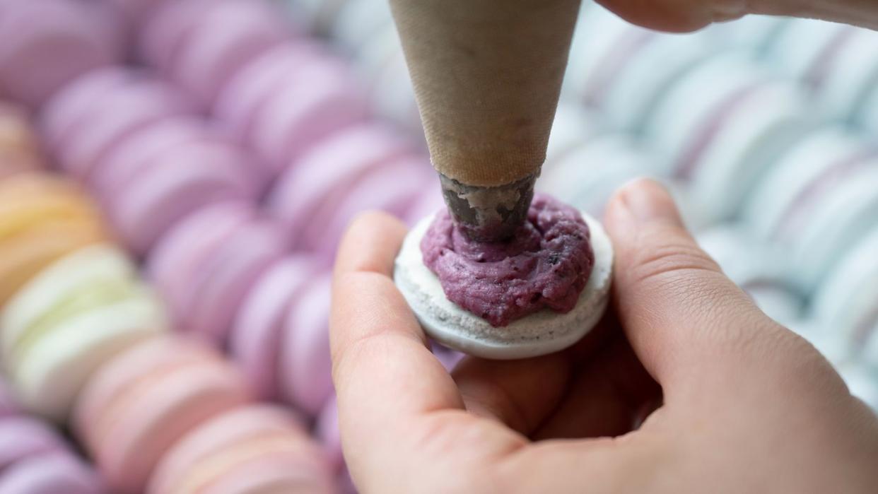 Ein Konditor befüllt Macarons (Bild: Sebastian Kahnert/dpa)