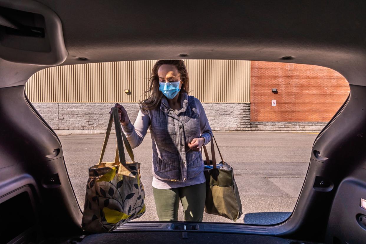 woman wearing a surgical mask and putting her purchases in her trunk