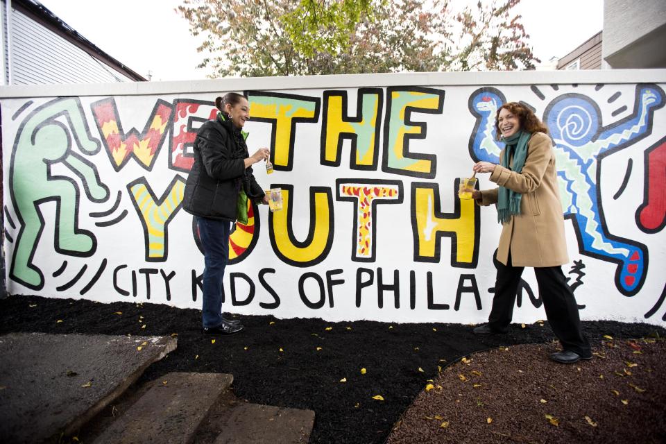 Julia Gruen, left, executive director of The Keith Haring Foundation, and Jane Golden, executive director of the Mural Arts Program, put the finishing brush strokes on the newly restored 1987 mural titled "We The Youth" by artist Keith Haring, Wednesday, Oct. 30, 2013, in the Point Breeze neighborhood of Philadelphia. The city’s Mural Arts Program has worked for months to restore the only collaborative public mural by Haring that is still intact and at its original site. Haring died of AIDS in 1990 at the age of 31. (AP Photo/Matt Rourke)