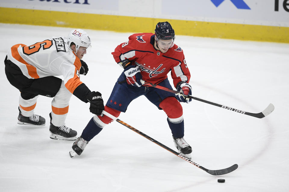 Philadelphia Flyers defenseman Travis Sanheim (6) reaches for the puck in front of Washington Capitals defenseman Dmitry Orlov (9) during the first period of an NHL hockey game Tuesday, April 13, 2021, in Washington. (AP Photo/Nick Wass)