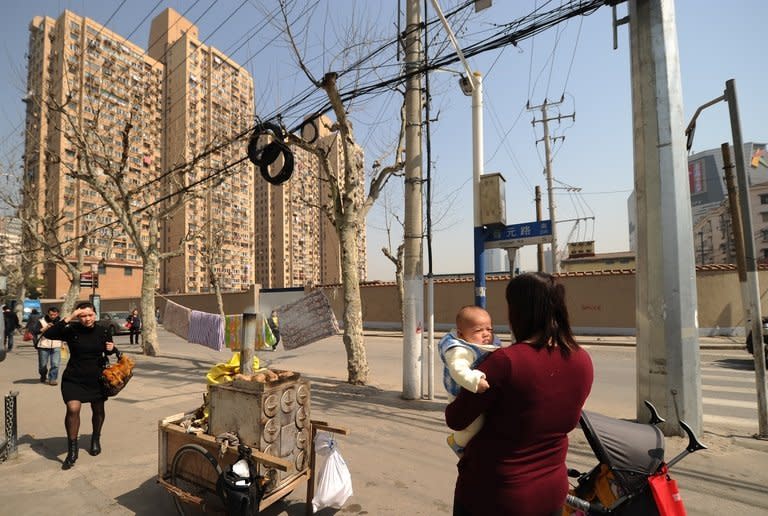 A woman holds her baby on a street in front of residential blocks in Shanghai on March 6, 2013. Chinese couples are flocking to divorce to avoid a new tax property sales tax imposed by the government, after it left open a loophole for those who end their marriages