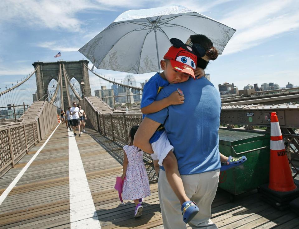 FILE - In this July 24, 2016, file photo, Xiuquin Huang carries her grandson Ruize Yan beneath an umbrella as she walks across the Brooklyn Bridge with her daughter and granddaughter Rina Wu. For the third straight year, Earth set a record for the hottest year, NOAA and NASA announced. NASA says 2016 was warmer than 2015 - by a lot. It's mostly global warming with a little assist from the now-gone El Nino. (AP Photo/Kathy Willens, File)