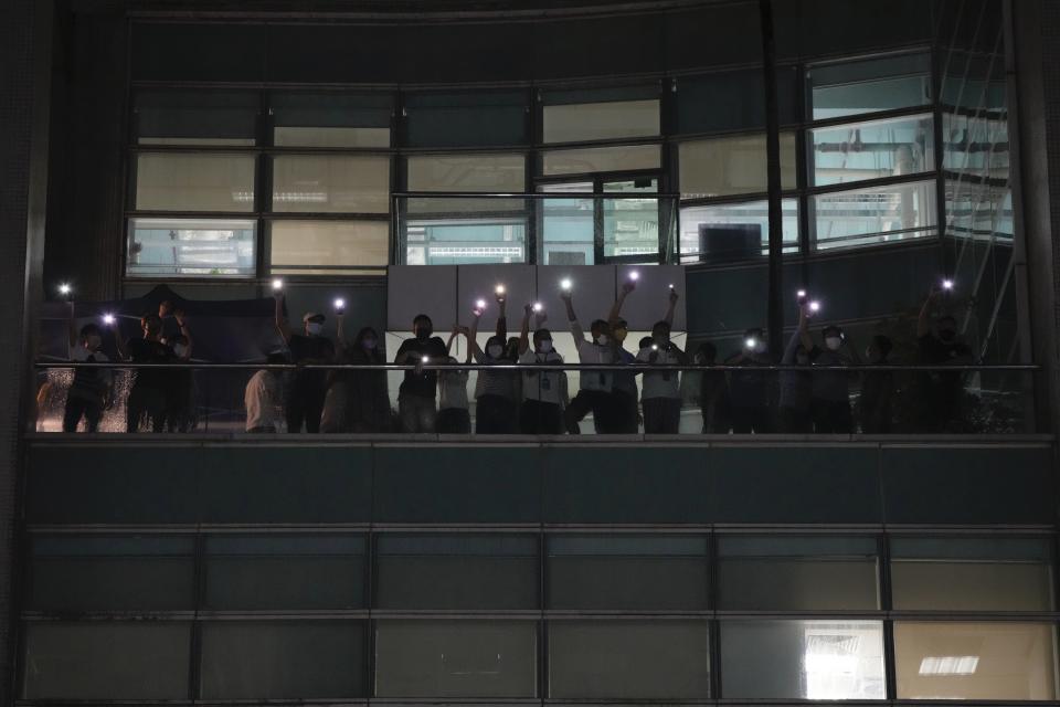 Staff members wave flashlights to their supporters at the Apple Daily headquarters in Hong Kong, Wednesday, June 23, 2021. Hong Kong's pro-democracy Apple Daily newspaper will stop publishing Thursday, following last week's arrest of five editors and executives and the freezing of $2.3 million in assets under the city's one-year-old national security law. (AP Photo/Kin Cheung)