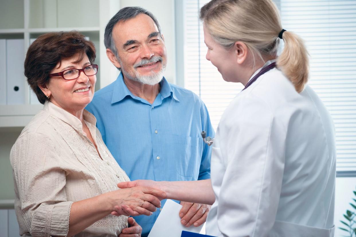 reassured senior couple smiling as doctor shakes their hands