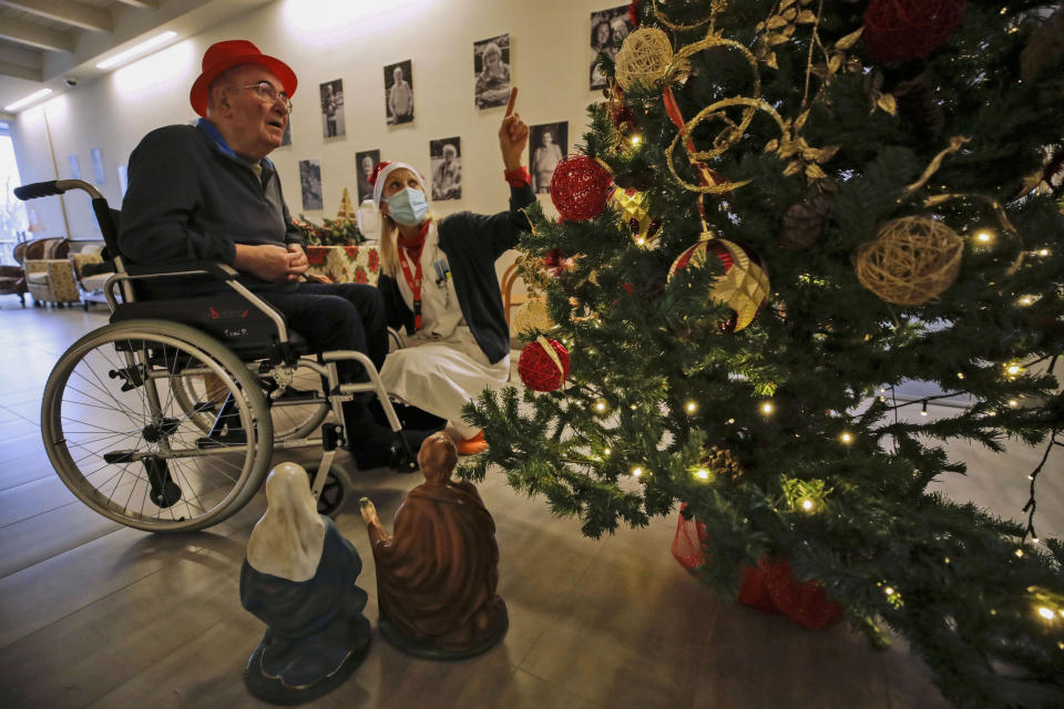 Palmiro Tami looks at a Christmas three flanked by director Maria Giulia Madaschi, before talking via video call with a donor unrelated to him who bought and sent him a Christmas present through an organization dubbed "Santa's Grandchildren", at the Martino Zanchi nursing home in Alzano Lombardo, one of the area that most suffered the first wave of COVID-19, in northern Italy, Saturday, Dec. 19, 2020. (AP Photo/Luca Bruno)