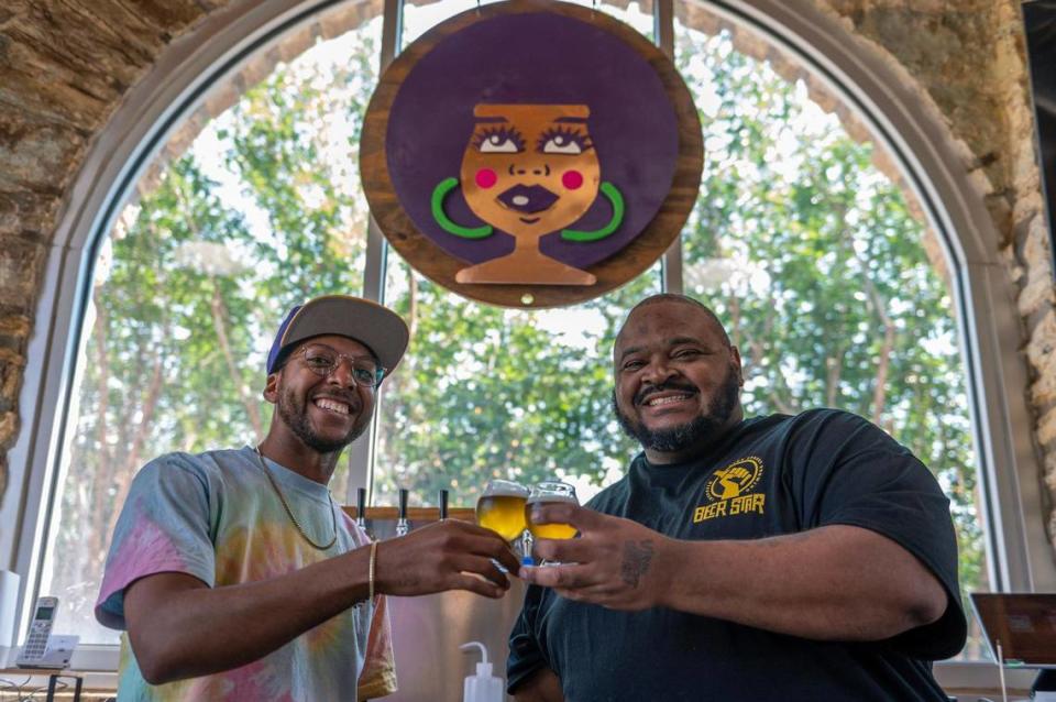 Kemet Coleman, left, and Woodie Bonds Jr., co-owners of Vine Street Brewing Co, share a toast beneath their brand’s logo, the beer goddess Maris.