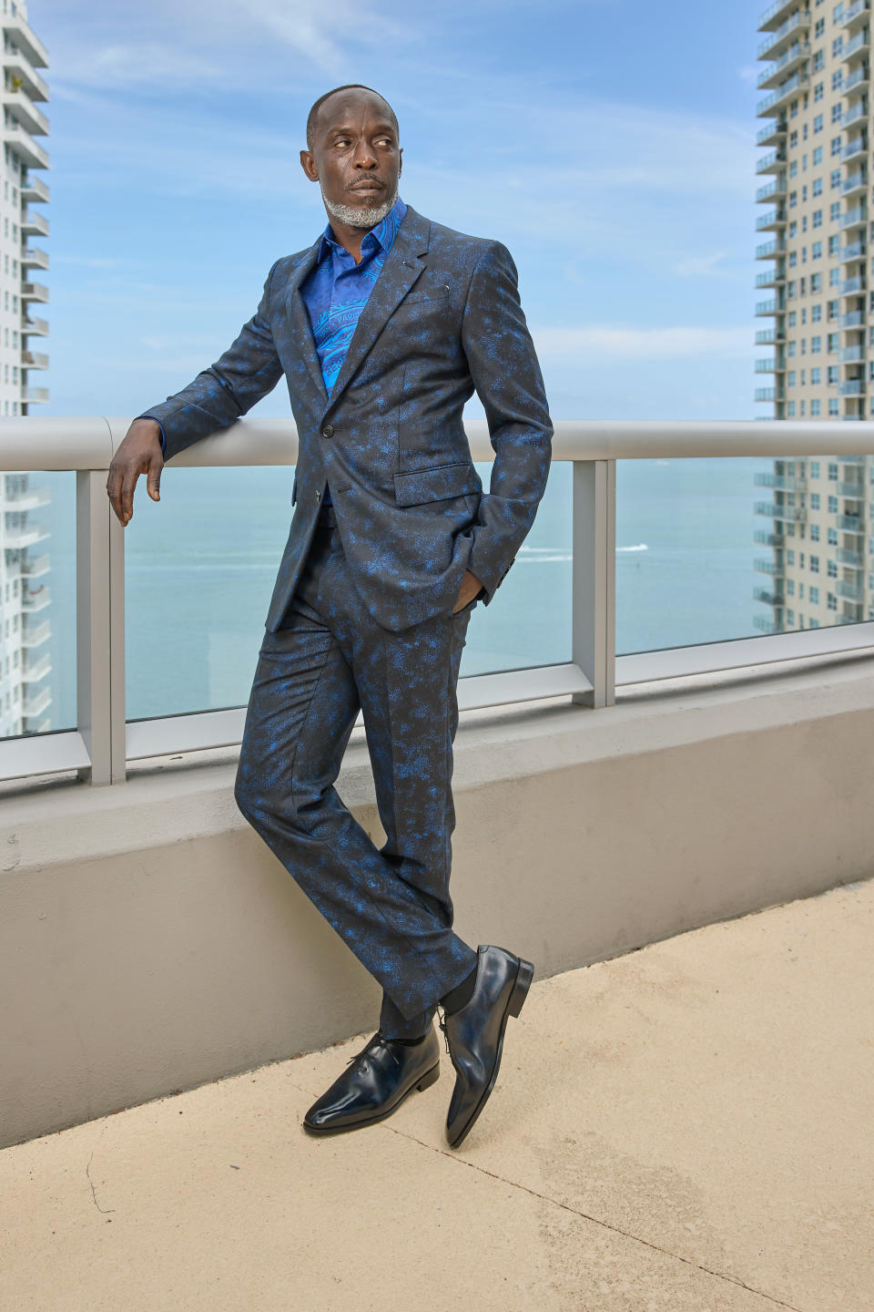 Michael wears a suit as he leans against a railing for a photo