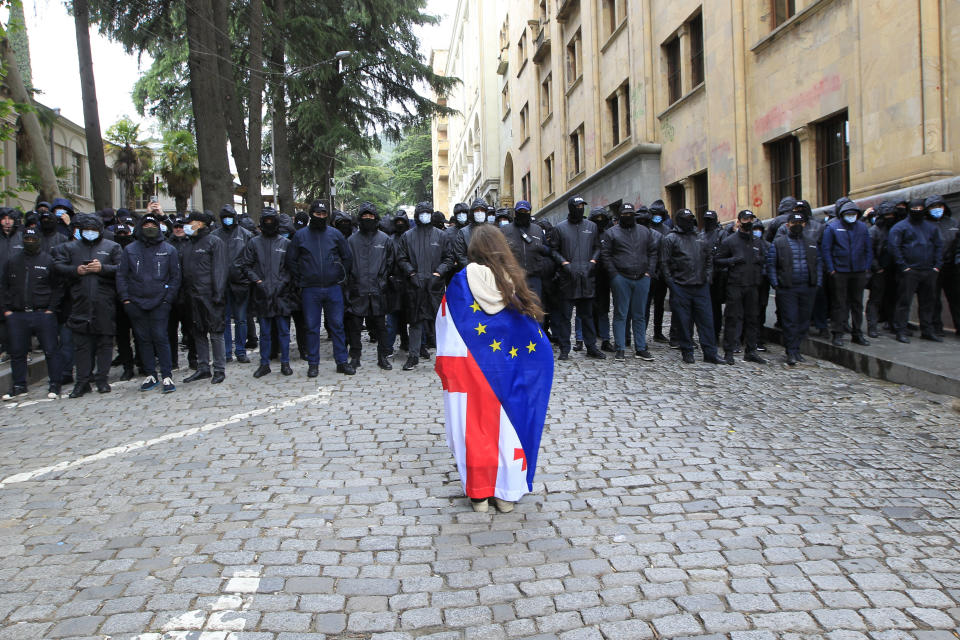 A demonstrator with draped Georgian national and EU flags stands in font of police blocking the way to the Parliament building, during an opposition protest against "the Russian law" in the center of Tbilisi, Georgia, Tuesday, May 14, 2024. Georgia's parliament on Tuesday began the third and final reading of a divisive bill that sparked weeks of mass protests, with critics seeing it as a threat to democratic freedoms and the country's aspirations to join the European Union. (AP Photo/Shakh Aivazov)