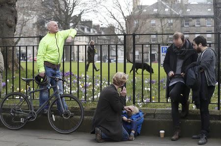 People listen and watch on their mobile devices as Scotland's First Minister Nicola Sturgeon demands a new independence referendum to be held in late 2018 or early 2019, once the terms of Britain's exit from the European Union have become clearer, outside Bute House, in Edinburgh, Scotland, Britain March 13, 2017. REUTERS/Russell Cheyne