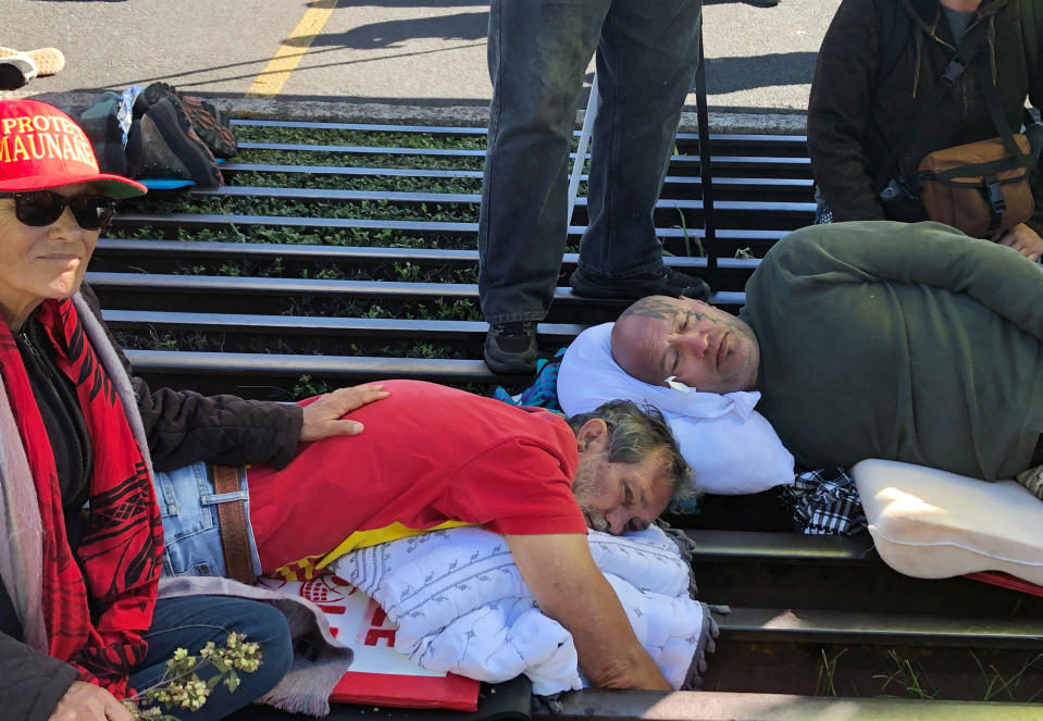 FILE - In this Monday, July 15, 2019, file photo, activist Walter Ritte, left, and others lie chained to a cattle grate blocking a road at the base of Hawaii's tallest mountain in Mauna Kea, Hawaii, protesting the construction of a giant telescope on land that some Native Hawaiians consider sacred. Ritte was in his early 30s when he became an activist for Native Hawaiian rights by fighting against military bombing on the island of Kahoolawe. Now at 74, he's still a prolific protester. (AP Photo/Caleb Jones, File)