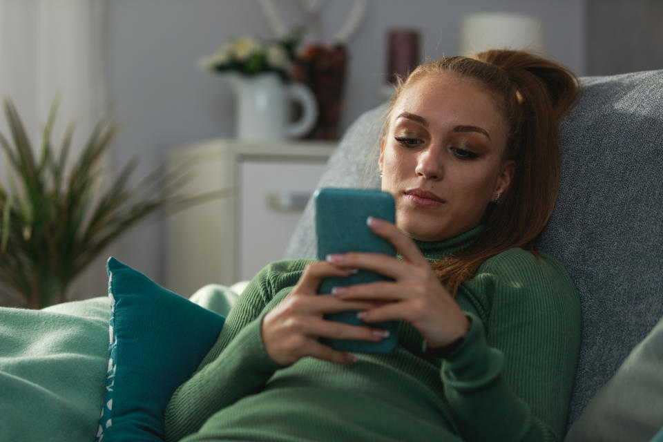 Imagen de una adolescente feliz descansando en el acogedor sofá de su sala de estar y enviando mensajes de texto a sus amigos a través de un teléfono inteligente. (Getty Creative)