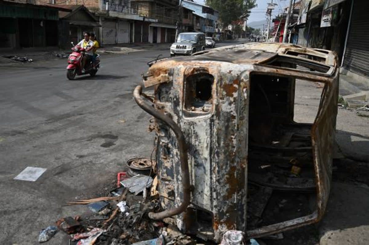 A motorist rides past a burnt vehicle on a street in Churachandpur in violence hit areas of northeastern Indian state of Manipur (AFP via Getty Images)
