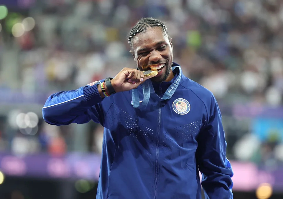 Gold medalist Noah Lyles pretends to bite his medal during a victory ceremony.