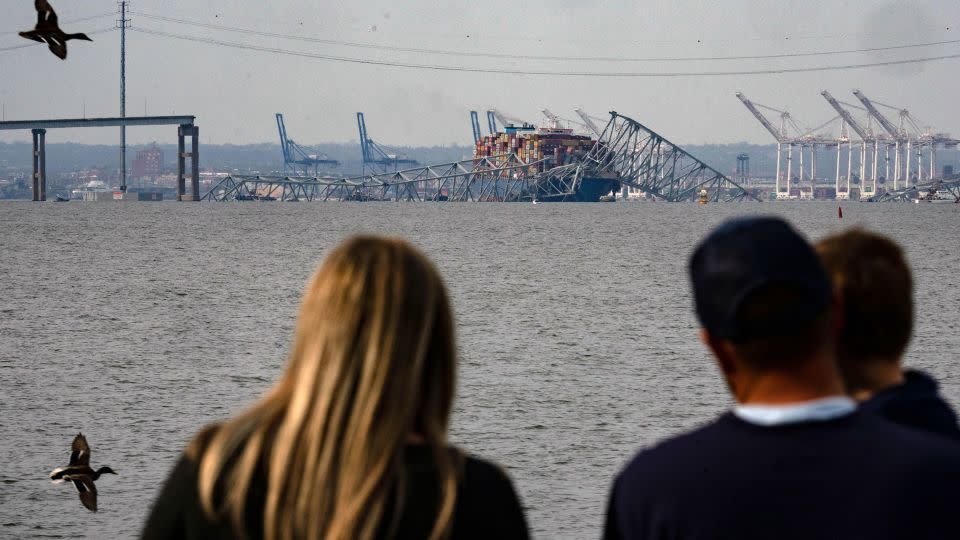 A family looks at the steel frame of the Key Bridge sitting on top of the container ship. - Kent Nishimura/AFP/Getty Images