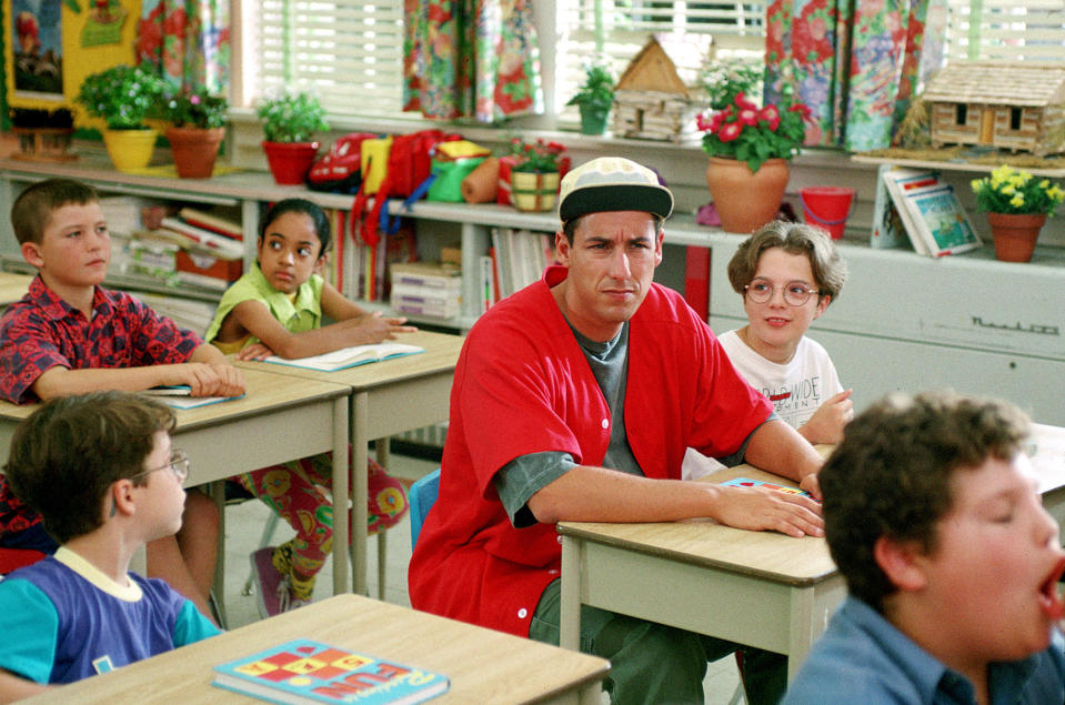 Adam Sandler sitting in an elementary school classroom surrounded by children