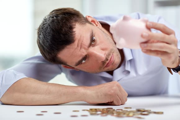 A man emptying his piggy bank and finding very little money.