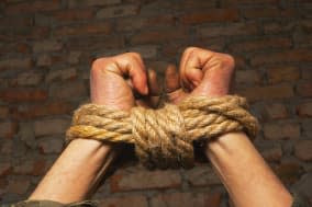 Hands tied up with rope against brick wall