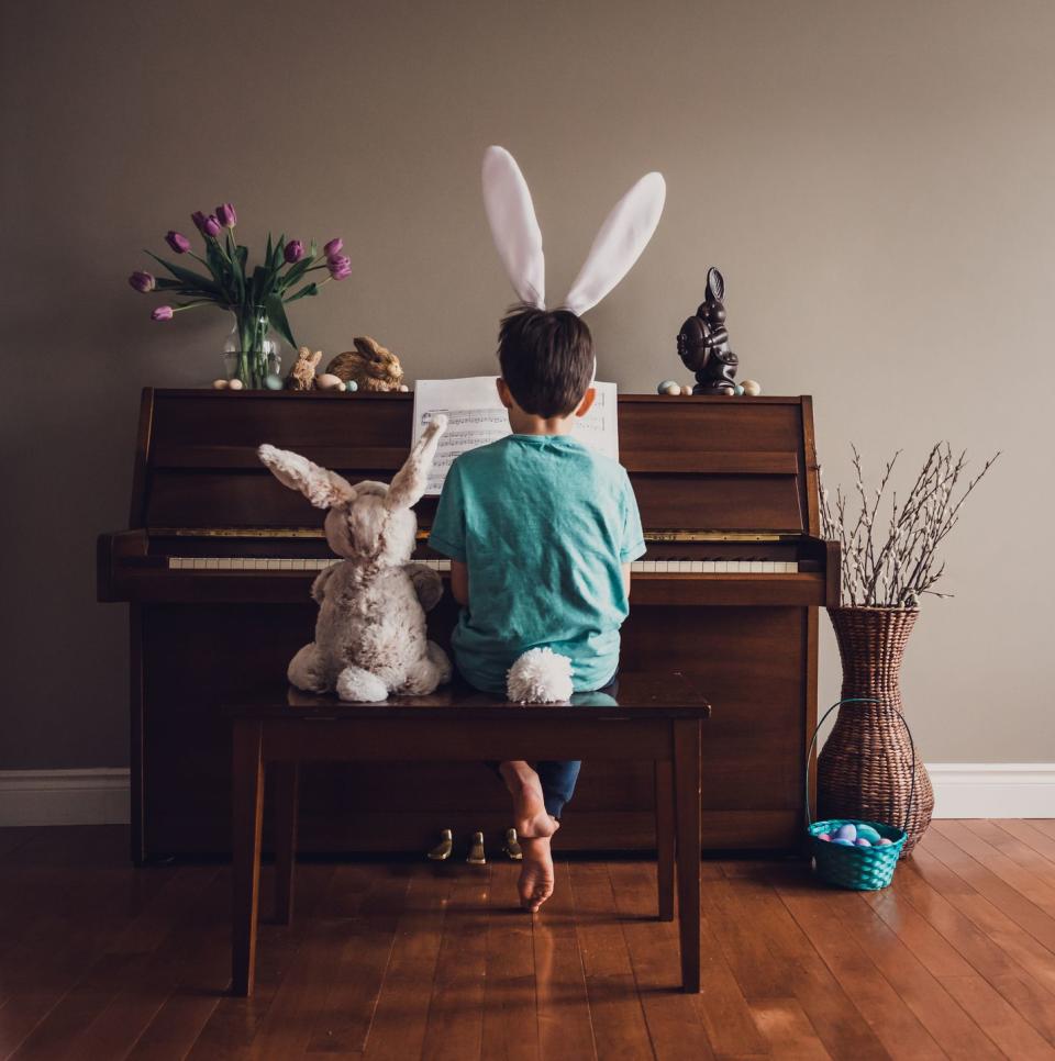 boy wearing bunny ears playing piano with a stuffed rabbit beside him