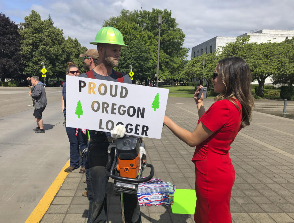 A TV reporter interviews self-employed logger Bridger Hasbrouck, of Dallas, Ore., outside the Oregon State House in Salem, Ore., on Thursday, June 20, 2019, the day the Senate is scheduled to take up a bill that would create the nation's second cap-and-trade program to curb carbon emissions. Senate Republicans, however, pledged to walk out so there wouldn't be enough lawmakers present for a vote on House Bill 2020, which is extremely unpopular among loggers, truckers and many rural voters. (AP Photo/Gillian Flaccus)