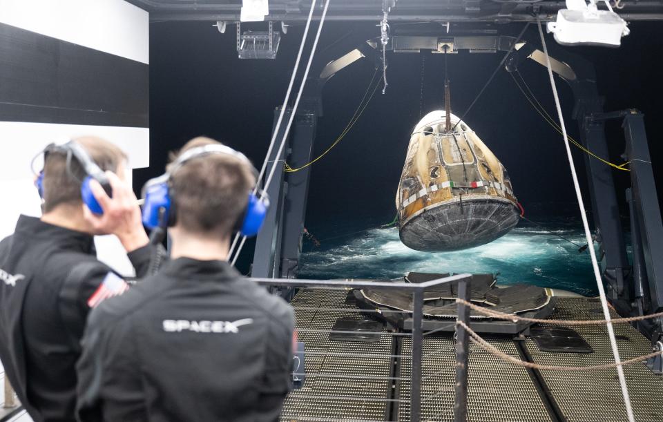 two people watch a space capsule load onto a ship