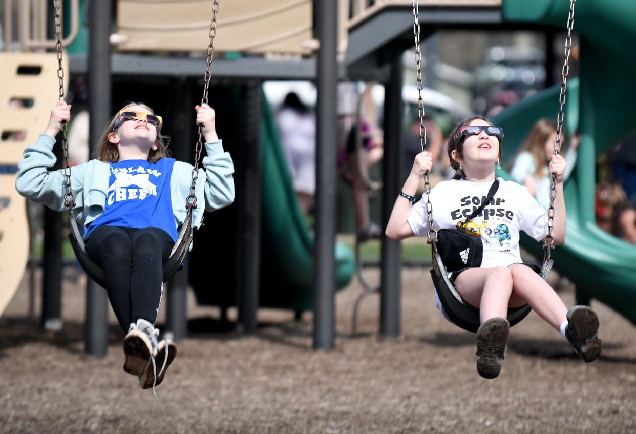 Brooklyn Hull, 11, and Hadly Gill, 10, both fifth grade students at Tuslaw, swing at St. Helena Heritage Park in Canal Fulton while watching the total solar eclipse Monday.