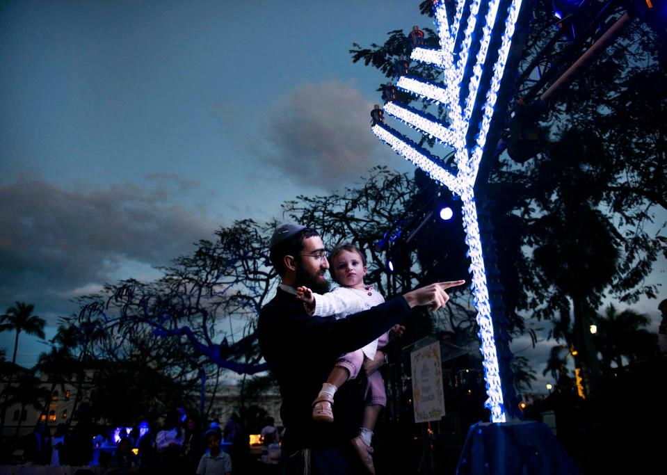 Rabbi Shneor Minsky shows his daughter Batya, 22 months, the "Israel Solidarity" menorah during the annual Hanukkah event at Bradley Park in Palm Beach, Fla.