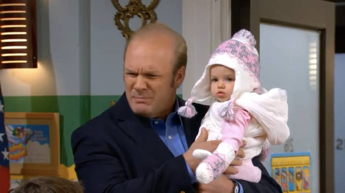 A man holds a baby dressed in a winter hat and mittens indoors. Both have focused expressions