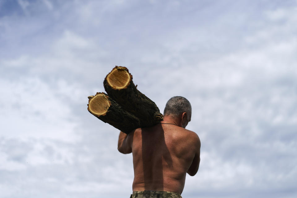 A member of the Dnipro-1 regiment carries a log to fortify a position near Sloviansk, Donetsk region, eastern Ukraine, Friday, Aug. 5, 2022. From a position on the outskirts of the city, soldiers with the Dnipro-1 regiment are expanding a network of trenches and digging bunkers capable of protecting soldiers against mortar strikes and phosphorous bombs. (AP Photo/David Goldman)