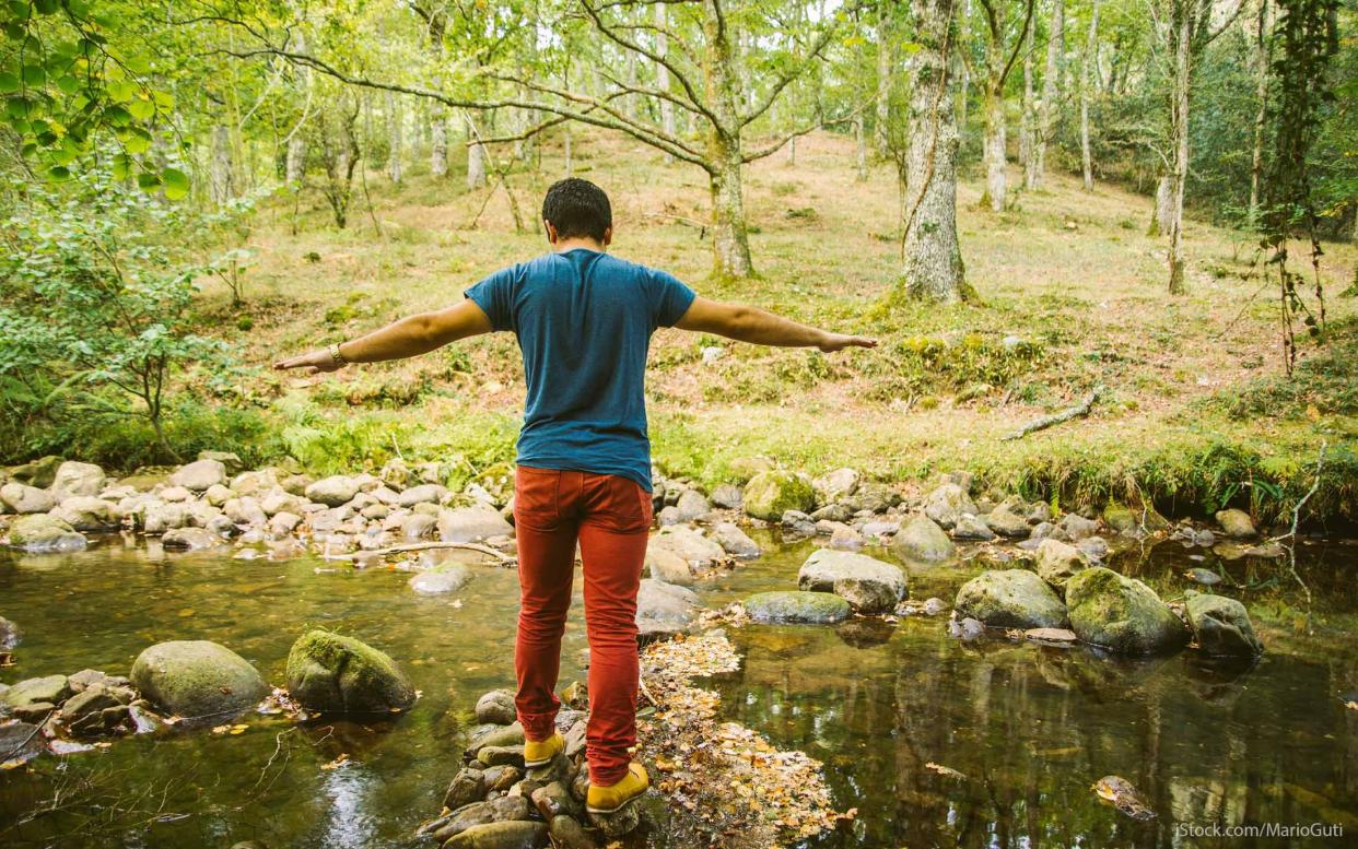 young man walking across a creek