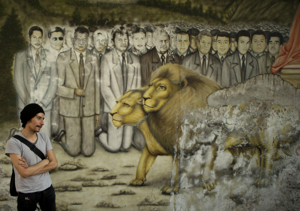 In this April 11, 2014 photo, actor Raul Briones stands in front of a mural depicting neighborhood residents killed by alcoholism and heart attacks as their souls prepare to meet Christ during a theater performance in the Tepito neighborhood of Mexico City. Many attending the production “Safari in Tepito” say it helped them better understand an area they would not have visited otherwise. (AP Photo/Rebecca Blackwell)