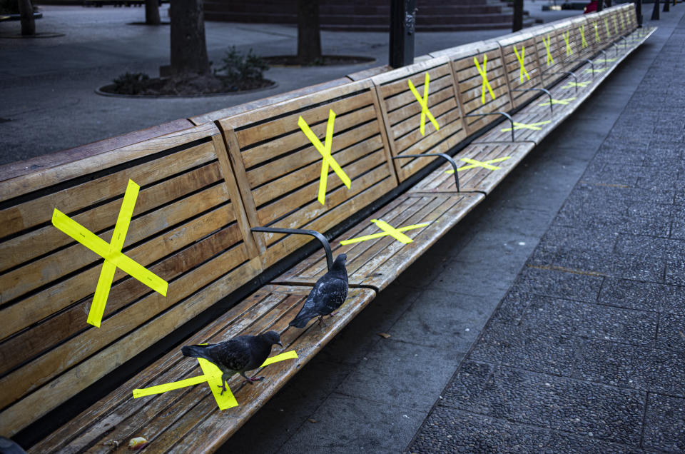 Pigeons walk along benches marked with X's, as a reminder to maintain a safe social distance, at the Plaza de Armas in Santiago, Chile, Saturday, June 12, 2021, amid the new coronavirus pandemic. The Chilean capitol has reinstated quarantine measures due to the increase in COVID-19 infections. (AP Photo/Esteban Felix)