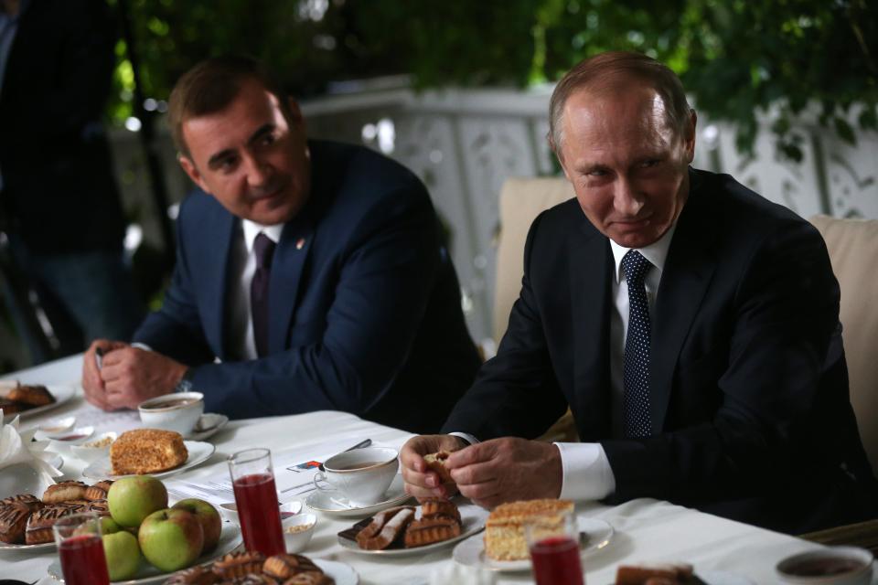 Two men sit side by side over a meal at an outdoor table.