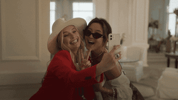 Two well-dressed women in a hotel lobby put their heads together to pose for a selfie