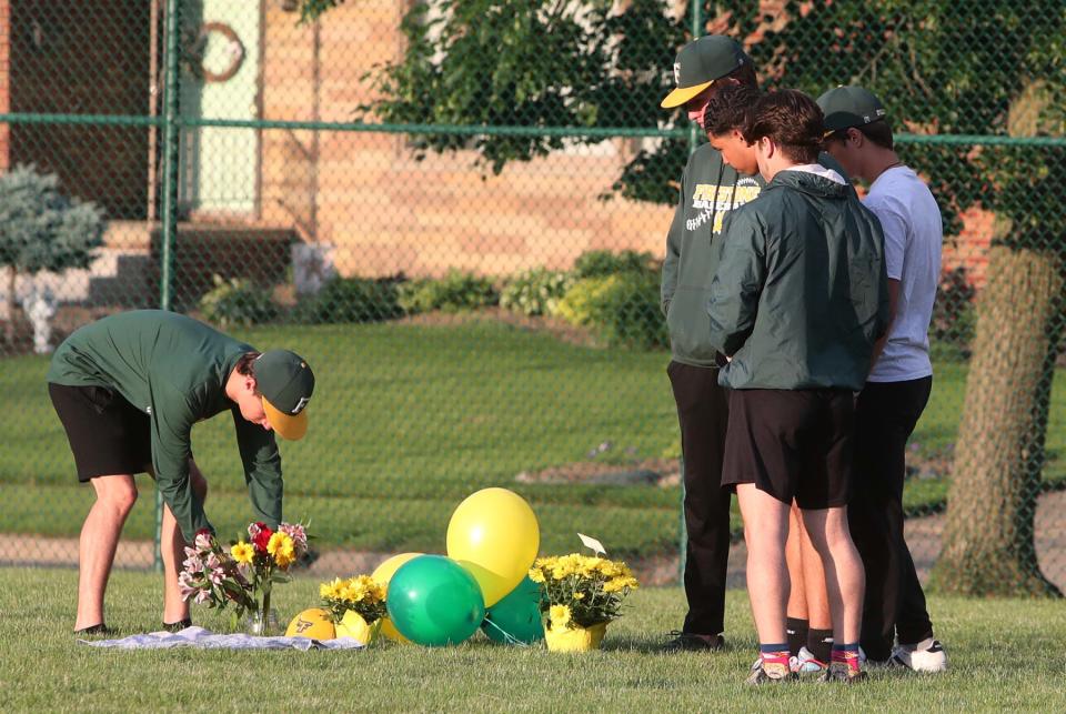 Teammates of Firestone High School outfielder Ethan Liming place flowers and balloons at his position in the outfield before a vigil at the school's baseball field for Liming Friday evening.