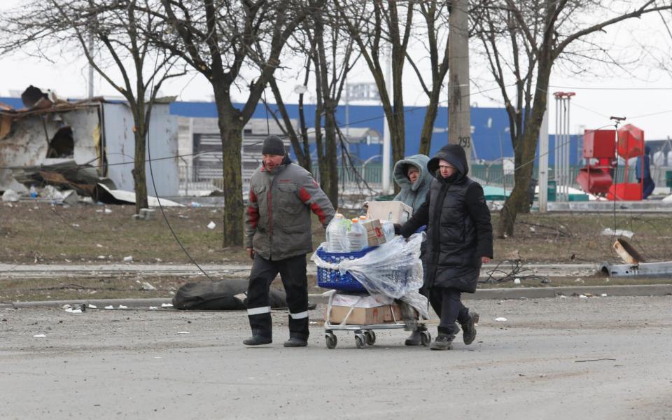 People push a cart filled with water bottles and food in the besieged city of Mariupol - Alexander Ermochenko/Reuters