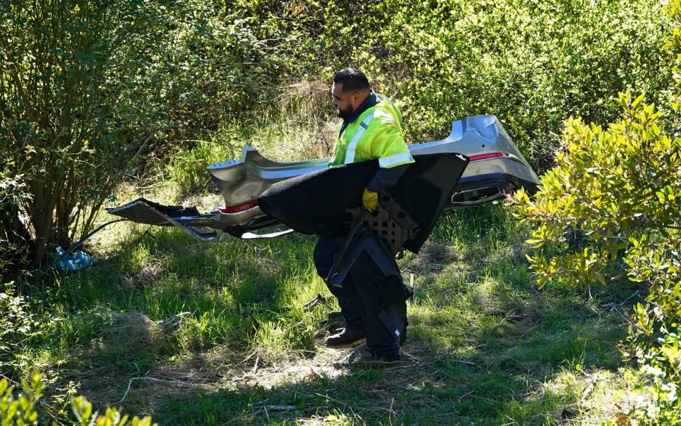 A worker moves debris after a rollover accident involving golfer Tiger Woods - AP