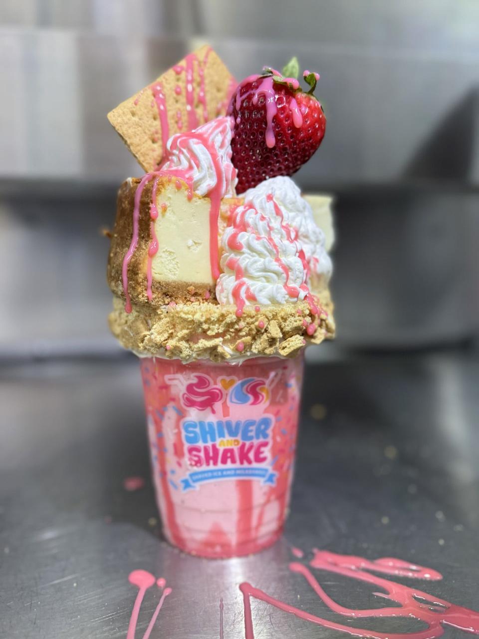 The strawberry cheesecake shake has a slice of cheesecake and a fresh strawberry topping the strawberry ice cream shake.