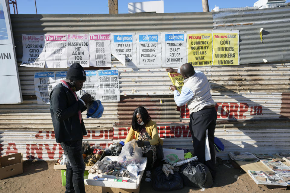 A vendor displays newspaper banners as a vendor prepares to sell, on a street, in Harare, Monday, July 25, 2022. Zimbabwe on Monday launched gold coins to be sold to the public to try to tame runaway inflation that has further eroded the country’s unstable currency. (AP Photo/Tsvangirayi Mukwazhi)