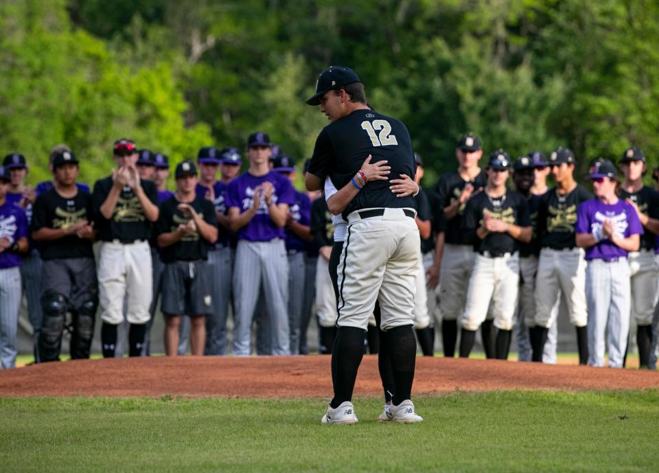 Buchholz High School baseball player Wyatt Clarke (12) gives Minde Reinhart a hug after she threw out the first pitch in honor of the Rex and Brody Foundation before the Buchholz and Gainesville High School game, Thursday, April 14, 2022, at Buchholz High School, in Gainesville, Florida. Reinhart set up the Foundation in her sons' honor after they were tragically killed by their father in a murder-suicide in May 2021. The boys were very active in baseball, and the Foundation was established to help fund youth baseball players who might not be able to afford it. It also helps fund scholarships and facility upgrades for local ball fields.
