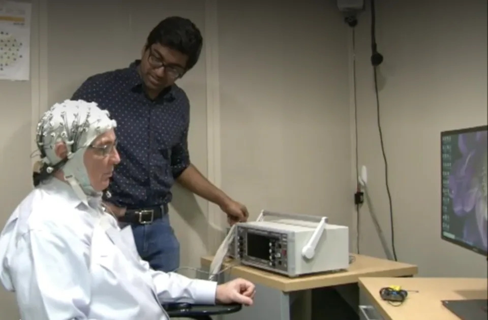 Volunteer Colin Riley receives noninvasive brain stimulation, as  Vighnesh Viswanathan looks on.